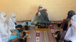 A tailoring trainer holds up a cloth while teaching the participants how to stitch during Aisha Azhar’s project